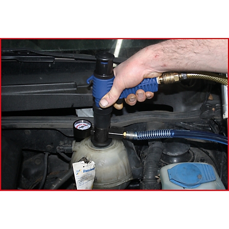 Mann befüllt Kühler eines Autos mit einem Werkzeug. Manometer und Schlauch sichtbar.